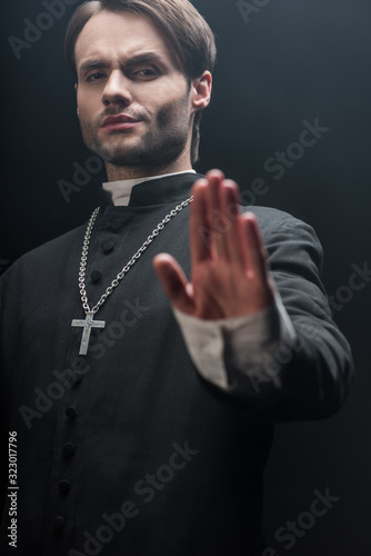 low angle view of strict catholic priest showing refuse gesture isolated on black