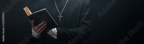Fotografia partial view of catholic priest reading holy bible isolated on black, panoramic