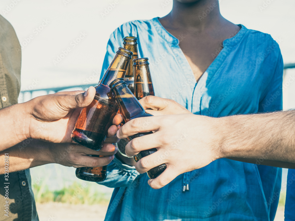 Naklejka premium Closeup shot of friends clinking beer bottles. Group of young people relaxing after work. Celebration concept