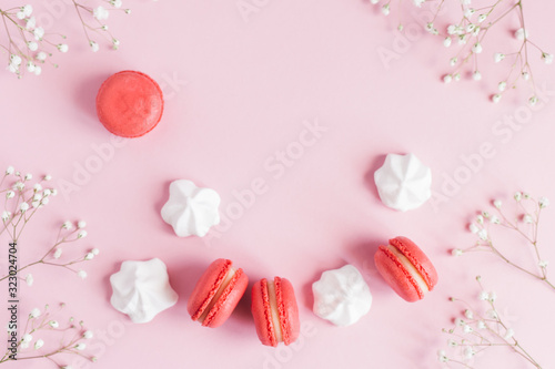 Pink macarons, white marshmallows and flowers on a pink pastel background.