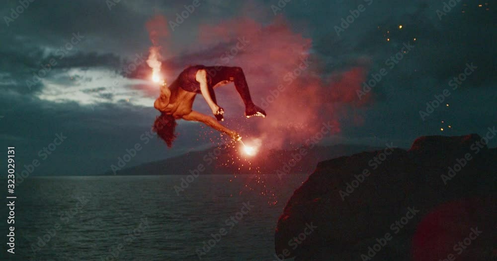 Extreme cliff jumping man backflipping off of an sea cliff with burning red hot flares at night, epic stuntman moments, people are awesome