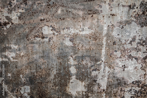 Rough textured cement concrete wall with varying shades of gray, brown and cream with peeling layers