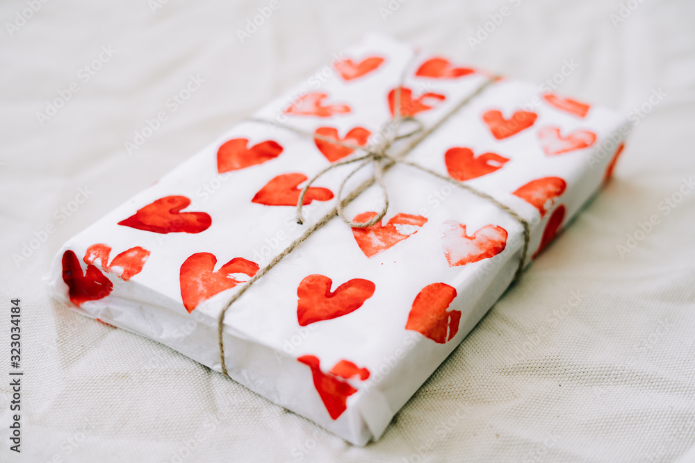 a gift wrapped in homemade wrapping paper with red hearts tied with jute thread for Valentine's day on a white table a gift wrapped in homemade wrapping paper with red hearts tied with jute thread for Valentine's day on a white table