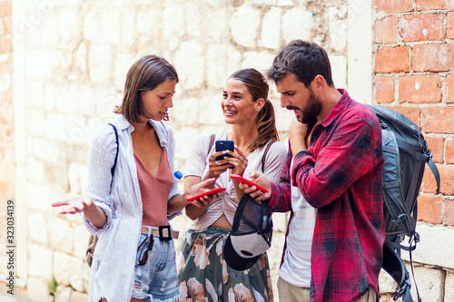 Happy group of three friends using a smartphone at street