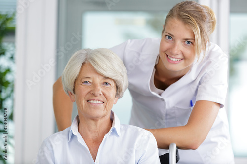 nurse supporting happy disabled senior woman in a wheelchair