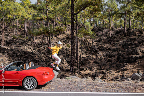 Young stylish woman traveling by car, jumpimg from the car trunk on the roadside in the forest. Carefree lifestyle and traveling concept photo