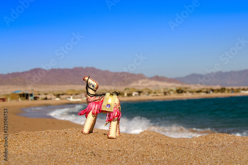 Egyptian United Arab Emirates UAE Morocco Israel souvenir camel arabic desert symbol on sand beach and sea background. Bright inanimate toy camel on the beach in the desert on the background