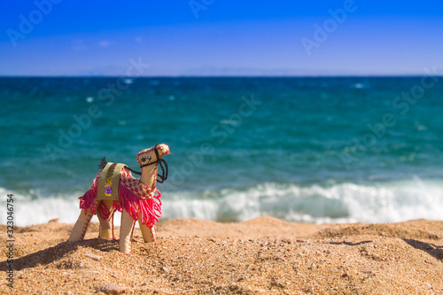 Egyptian Arab UAE Morocco Israel Egyptian souvenir camel arabic desert symbol on sand beach and sea background. Bright inanimate toy camel on the beach on the shores of the red sea near the water
