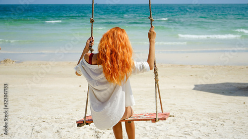 Beach summer vacation tropic palm style portrait of young beautiful girl on beach swing blue sea.Red haired woman swinging on the beach on Phu Quoc island, Vietnam. Happy  on tropical palm tree swing.