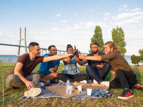 Happy people cheering with beer and eating pizza. Good friends resting at nature. Concept of picnic