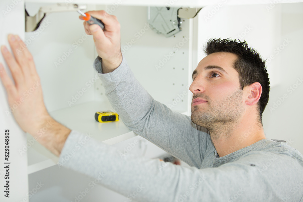Fototapeta premium handyman fixing a door on the cupboard