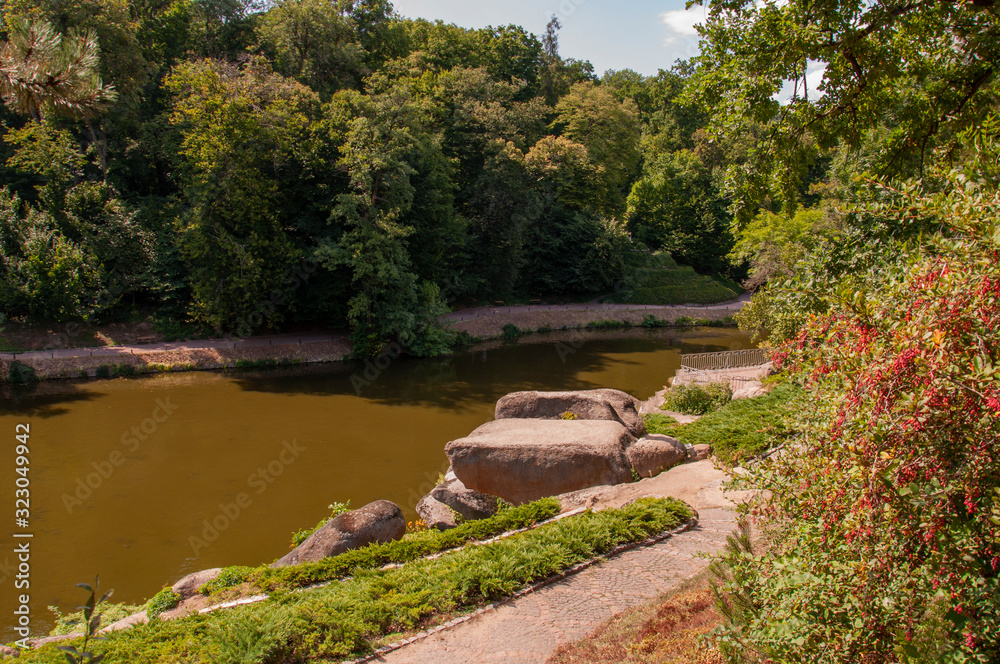 Beautiful nature landscape park with green herbs and trees, big stones and little river with waterfall in summer Beautiful nature landscape park with green herbs and trees, big stones and little river with waterfall in summer