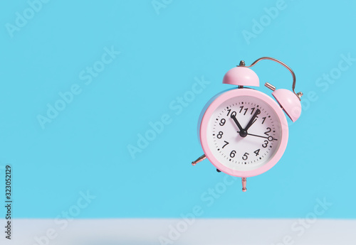 Pink alarm clock flies in the air on a blue background. Levitation effect