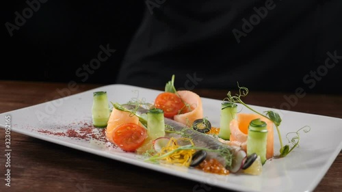 Food footage in slow motion. Delicious sliced herring served on plate with cucumbers and vegetables. Chef sprinkles pepper on plate. Restaurant food serving. Full hd