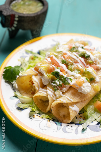 Mexican potato and cheese fried tacos also called flautas with green sauce on turquoise background