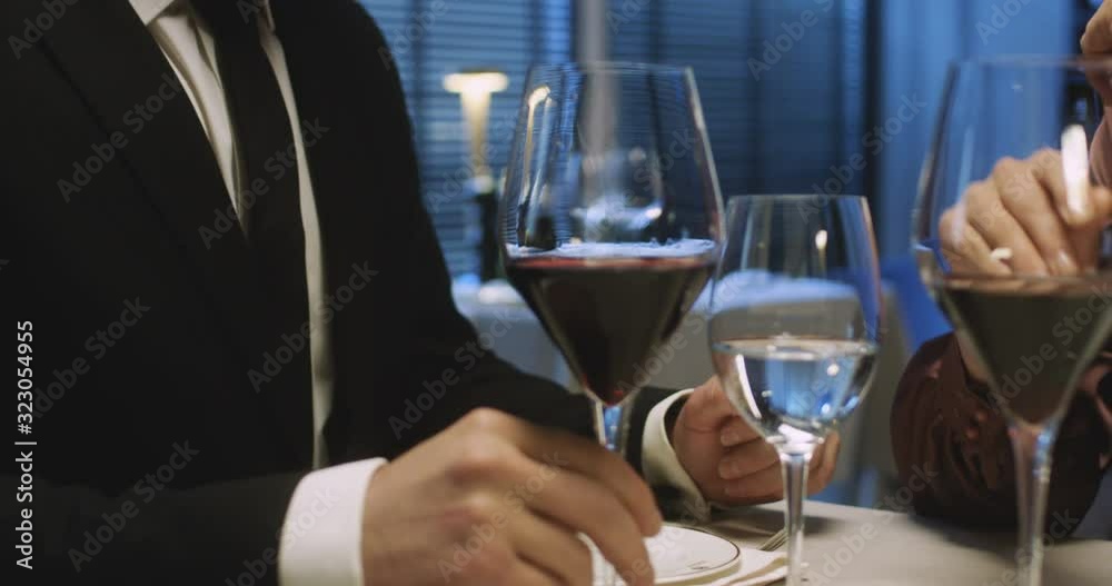 Close up of Caucasian man and woman having dinner in restaurant on date. Male and female hands puttung glasses with red wine on table and touching with love while holding. Romantic couple concept. Close up of Caucasian man and woman having dinner in restaurant on date. Male and female hands puttung glasses with red wine on table and touching with love while holding. Romantic couple concept.