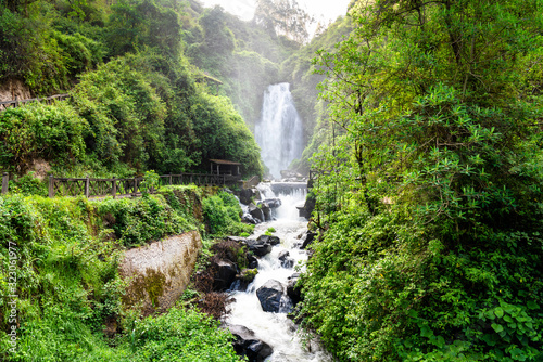 View of Peguche Waterfall in the mountains of Ecuador. It's surrounded by green forest full of vegetation photo