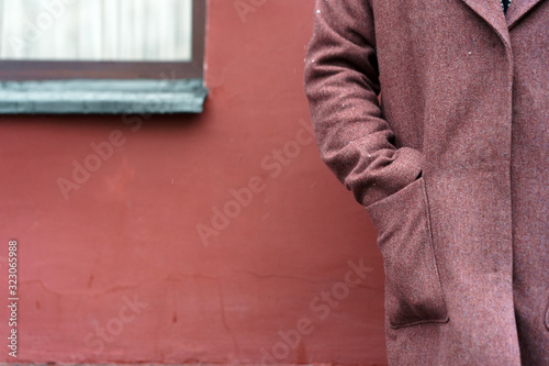 Portrait of a woman hand in the pocket in a burgundy coat view from the back against a red wall. The concept of minimalism in composition, without a face. Impersonal. Winter snowflake 