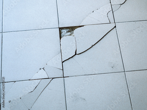 Close-up photo of light gray tile with large diagonal cracks and chips. photo