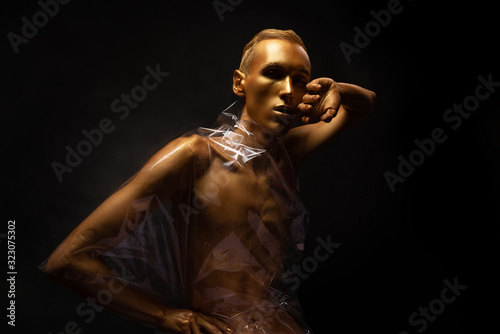 Man in gold paint. Guy fashion model beauty shot Shiny body art paint gold on a black background.
