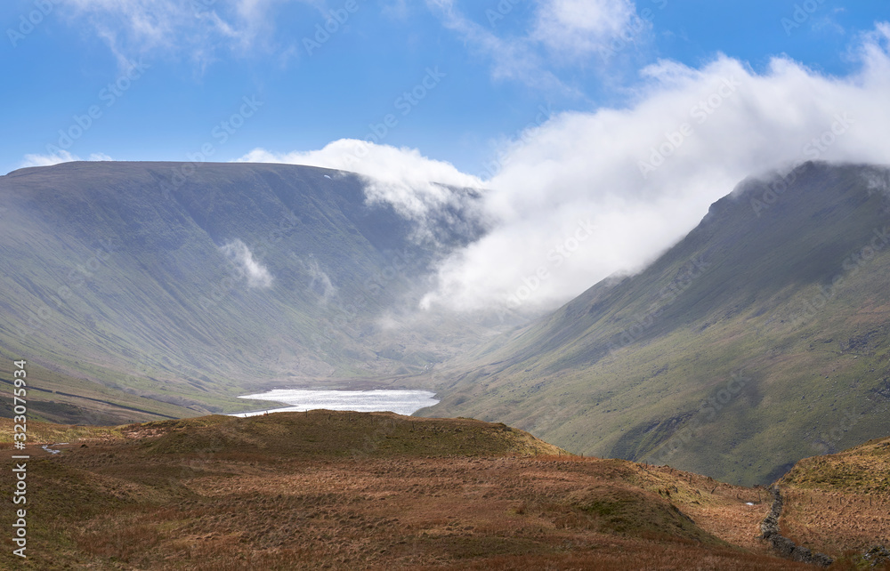 Distant views of Hayeswater Reservoir below the mountain summits of High Street, Thornthwaite (in the cloud) and Gray Crag on the right in the Lake District UK. Distant views of Hayeswater Reservoir below the mountain summits of High Street, Thornthwaite (in the cloud) and Gray Crag on the right in the Lake District UK.