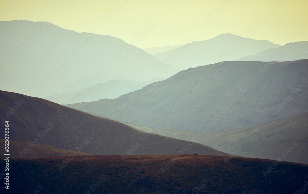 A compressed mountain view of ridges in the evening mist just before sunset from the summit of Rampsgill Head in the Lake District.