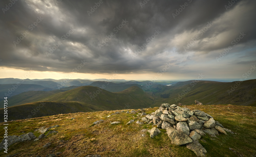 Dark clouds gather over the mountains in the evening just before sunset from the summit of Rampsgill Head with Rest Dodd, The Nab and Martindale Common in the in the Lake District.