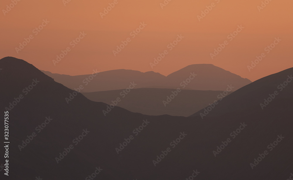The warm late evening glow of sunset over the mountains of the Lake District with the sun just just after the sun dipped below the ridgeline.