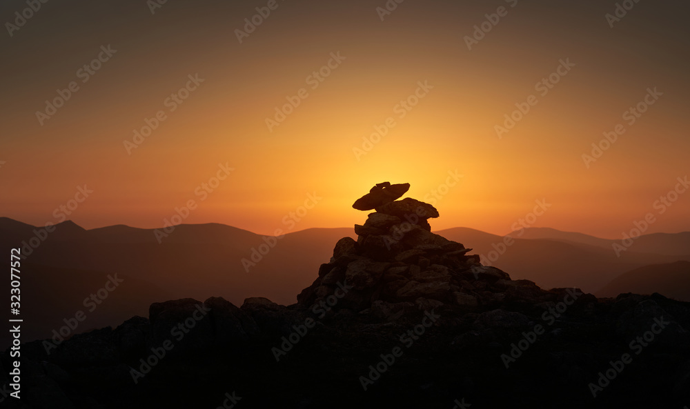 The warm evening sunlight of the mountain summit cairn of Rampsgill Head at sunset in the Lake District UK.