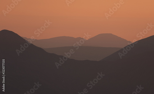 The warm late evening glow of sunset over the mountains of the Lake District with the sun just just after the sun dipped below the ridgeline.