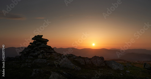 The warm evening sunlight of the mountain summit cairn of Rampsgill Head at sunset in the Lake District UK.