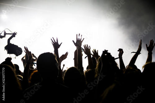 Stage lights and crowd of audience with hands raised at a music festival. Fans enjoying the party vibes.