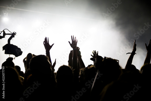 Fototapeta Stage lights and crowd of audience with hands raised at a music festival