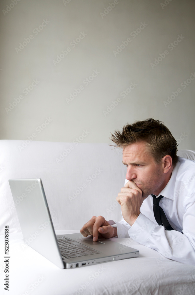 Man in smart casual unbuttoned white shirt lying on white sofa with his laptop computer 