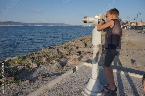 Quadro su tela A boy looks through a telescope at sea, a concept of tourism and entertainment
