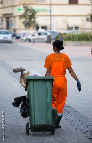 Фотография Garbage worker pulling trash can in street