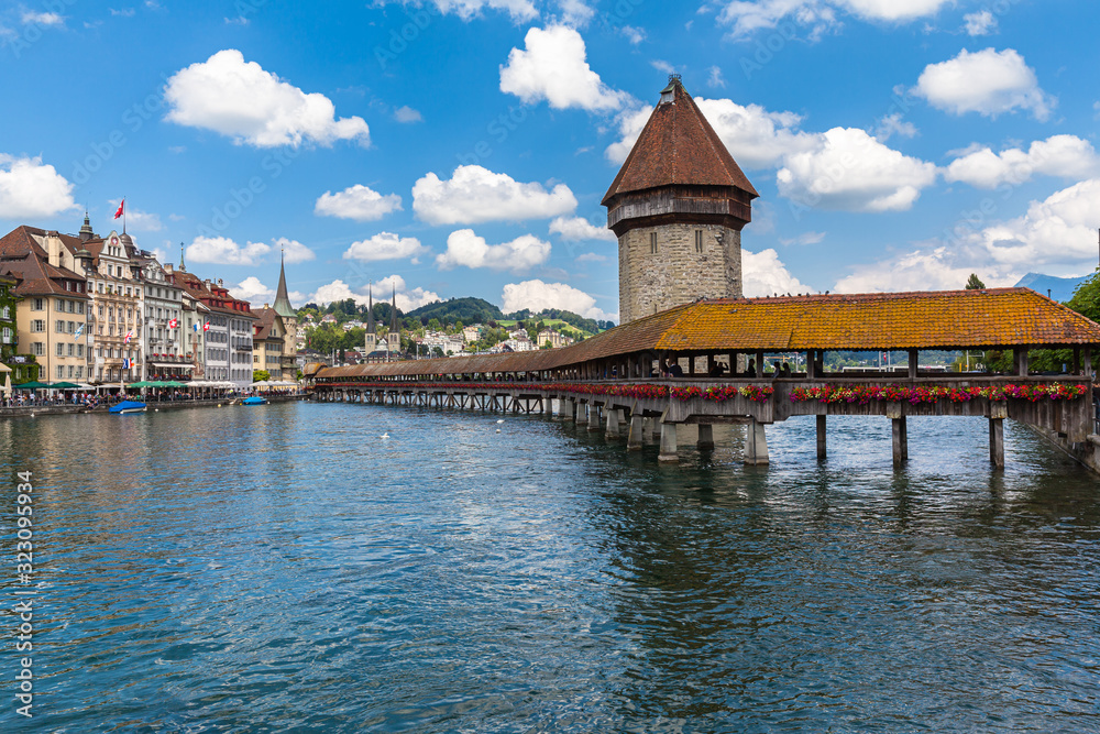Beautiful view of Chapel Bridge (Kapellbruecke) and Water Tower (Wasserturm) with Lucerne old town in background and Reuss river flowing to lake, on sunny summer day with blue sky cloud, Switzerland