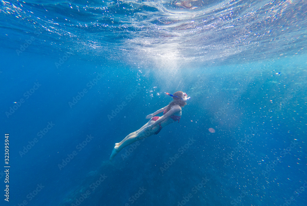 Girl with a mask and a snorkel dives into the sea with corals and fish
