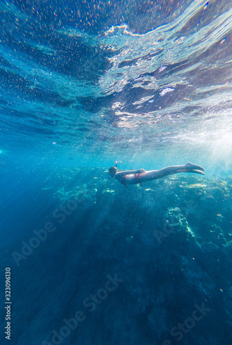 Girl with a mask and a snorkel dives into the sea with corals and fish