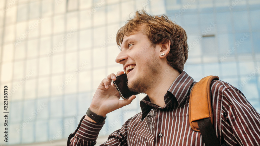 Young man talking on smartphone on the street near business center. Businessman makes an appointment and conduct preliminary negotiations. Man using smart watch app. Business and digital technology. Young man talking on smartphone on the street near business center. Businessman makes an appointment and conduct preliminary negotiations. Man using smart watch app. Business and digital technology.