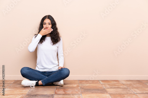 Young woman sitting on the floor covering mouth with hands