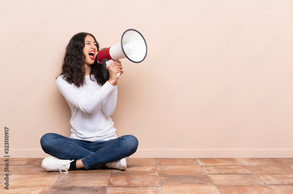 Young woman sitting on the floor shouting through a megaphone Young woman sitting on the floor shouting through a megaphone