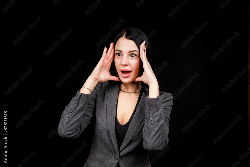 Young woman is angry. The girl wear casual grey jacket on a black background. Evil woman, hands on her sides
