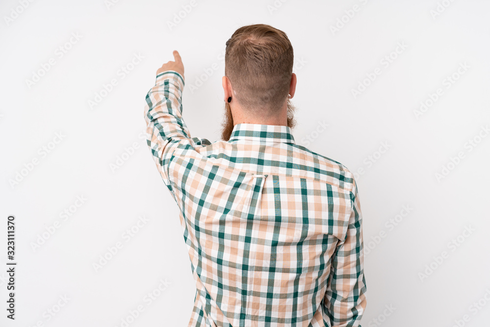 Redhead man with long beard over isolated white background pointing back with the index finger Redhead man with long beard over isolated white background pointing back with the index finger