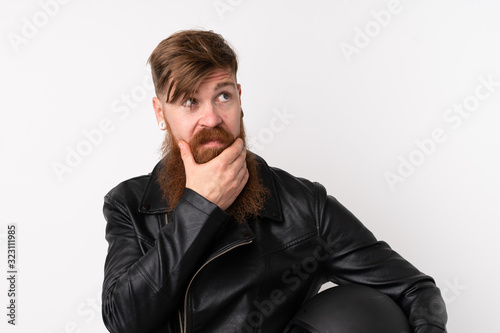 Redhead man with long beard holding a motorcycle helmet over isolated white background standing and looking to the side