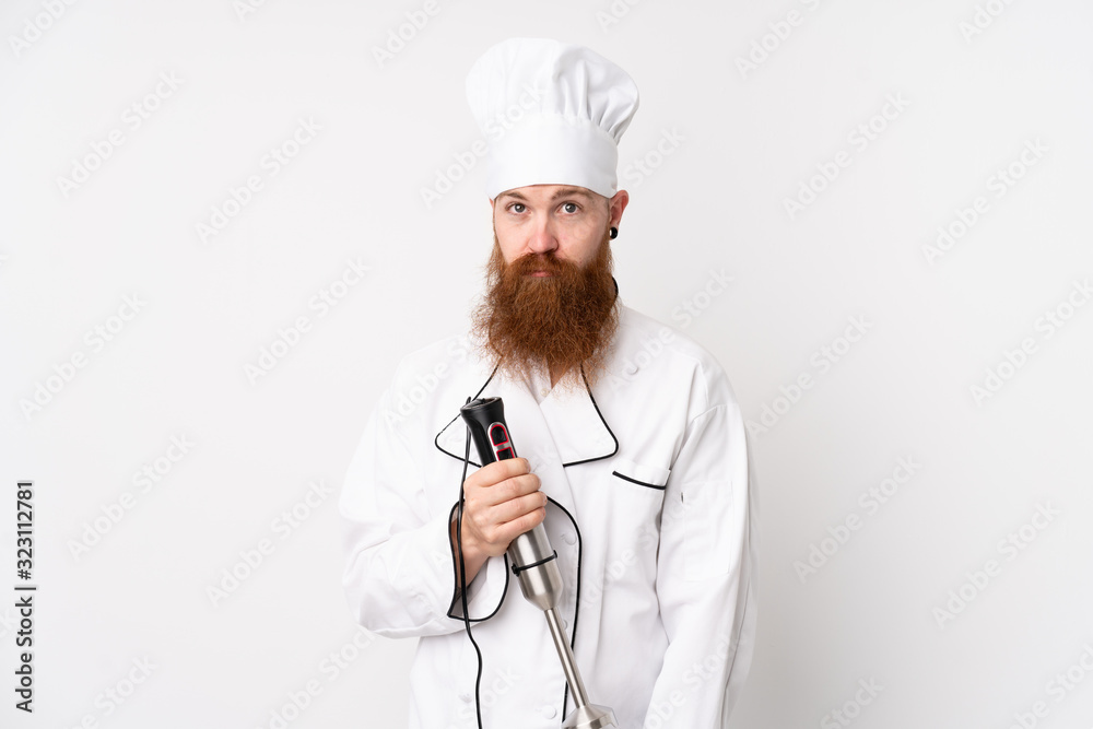 Redhead man using hand blender over isolated white background sad