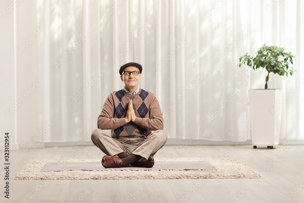 Senior man sitting on a mat with crossed legs meditating