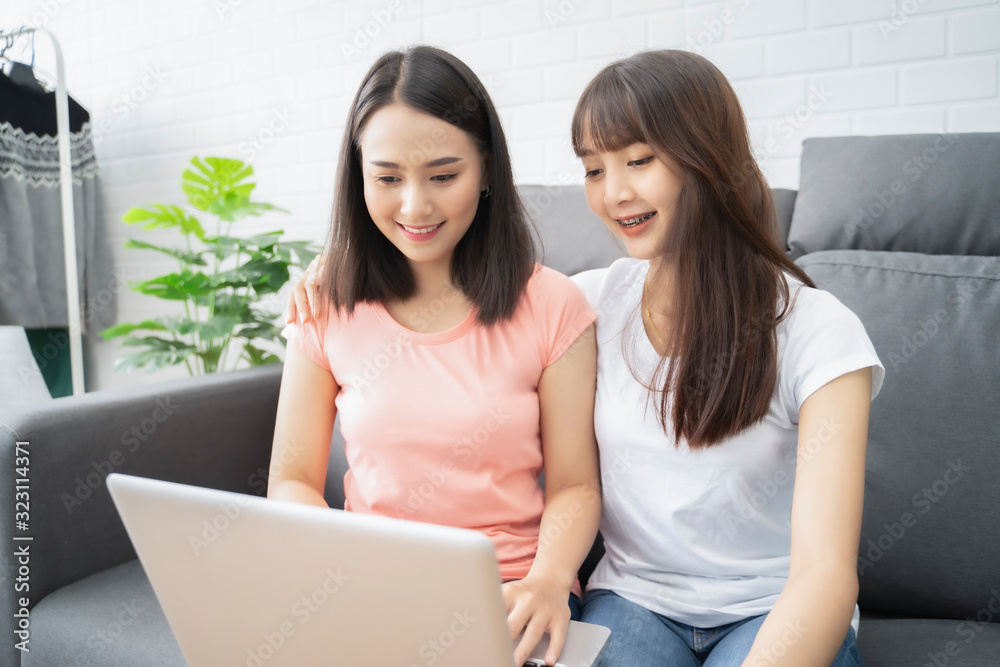 Asian women couple two LGBT lesbian happy couple sitting near a sofa using a laptop computer, phone for shopping online in the living room at home. LGBT lesbian couple community together concept. Asian women couple two LGBT lesbian happy couple sitting near a sofa using a laptop computer, phone for shopping online in the living room at home. LGBT lesbian couple community together concept.