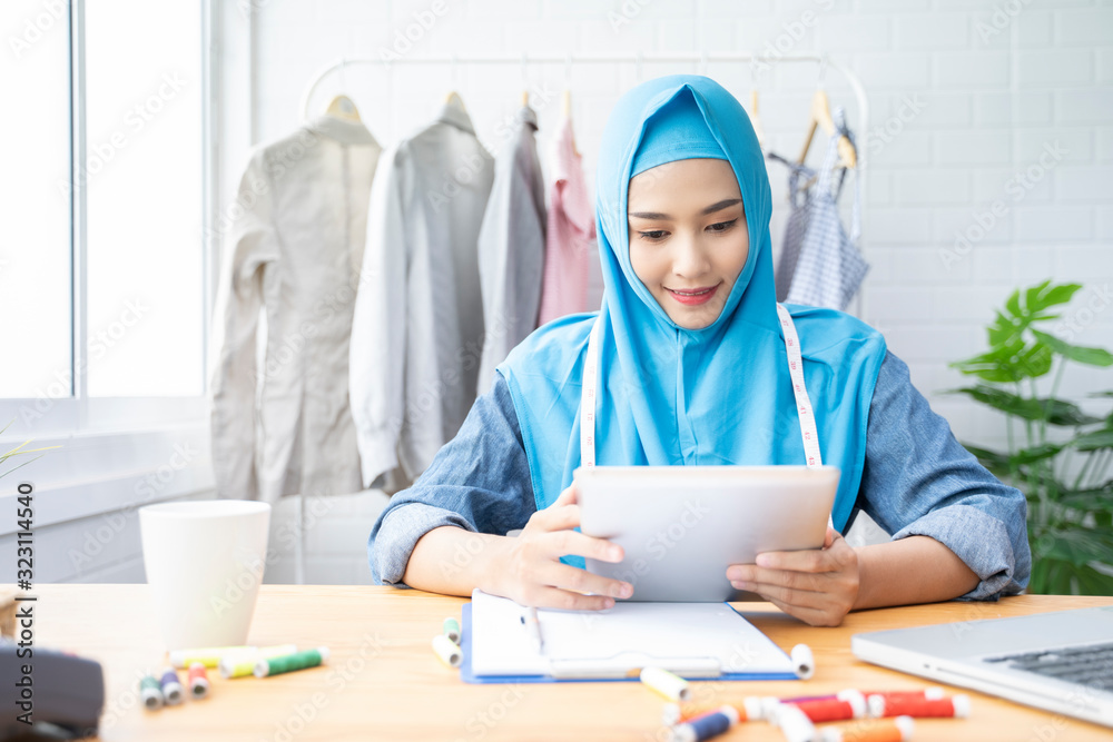 Beautiful Muslim businesswoman smile with digital tablets checking stock in her fashion boutique, female owner Muslim woman fashion designer work in her workshop, looking to tablets Beautiful Muslim businesswoman smile with digital tablets checking stock in her fashion boutique, female owner Muslim woman fashion designer work in her workshop, looking to tablets