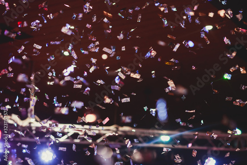 Colourful confetti explosion fired on dance floor air during a concert festival  crowded concert hall with scene stage lights  rock show performance  with people silhouette